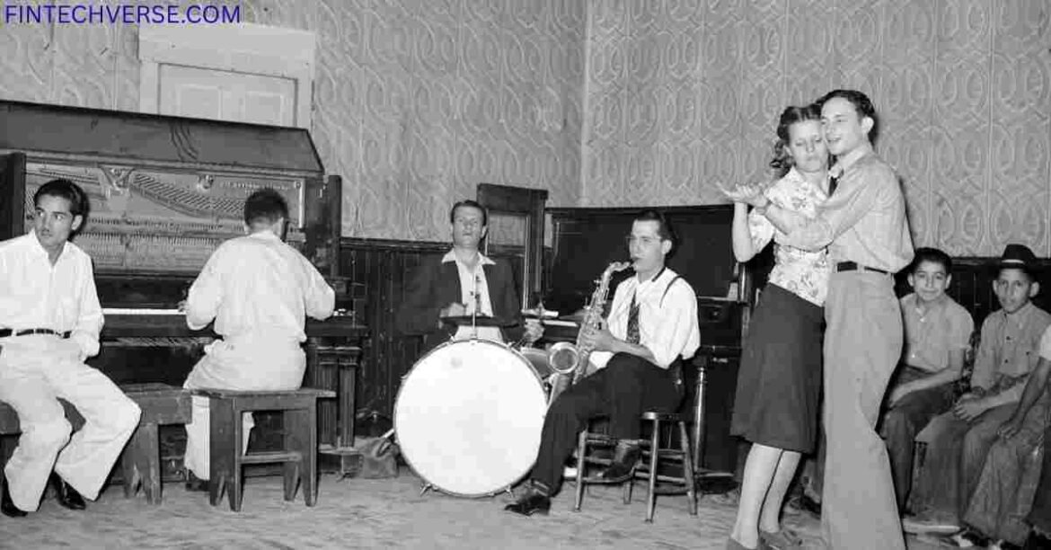Black and white photo of a vintage dance hall scene with live band playing music. Two people are dancing in the center, while others sit and watch. The band includes a pianist, drummer, and saxophonist, with an upright piano in the background.